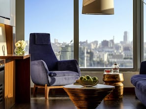 A modern living room with a city view, a blue armchair, a wooden coffee table, and a vase of flowers.