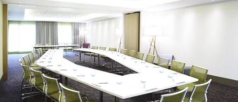 Sala de conferências com uma mesa comprida, cadeiras verdes e um quadro branco.