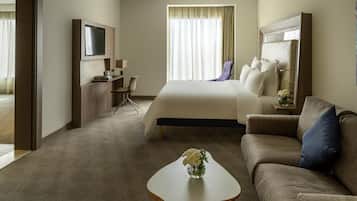 Habitación de hotel con cama, sofá, televisión, escritorio y mesa de centro con flores.