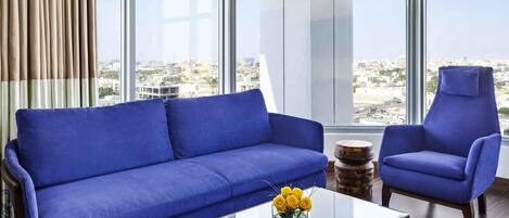 Una sala de estar moderna con un sofá azul, un sillón a juego y una mesa de centro de vidrio con flores amarillas.