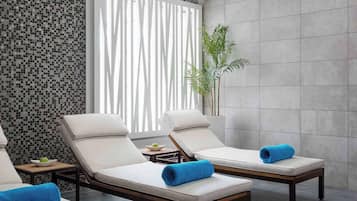 Relax in a serene spa room with two lounge chairs, a potted plant, and a mosaic tile wall.