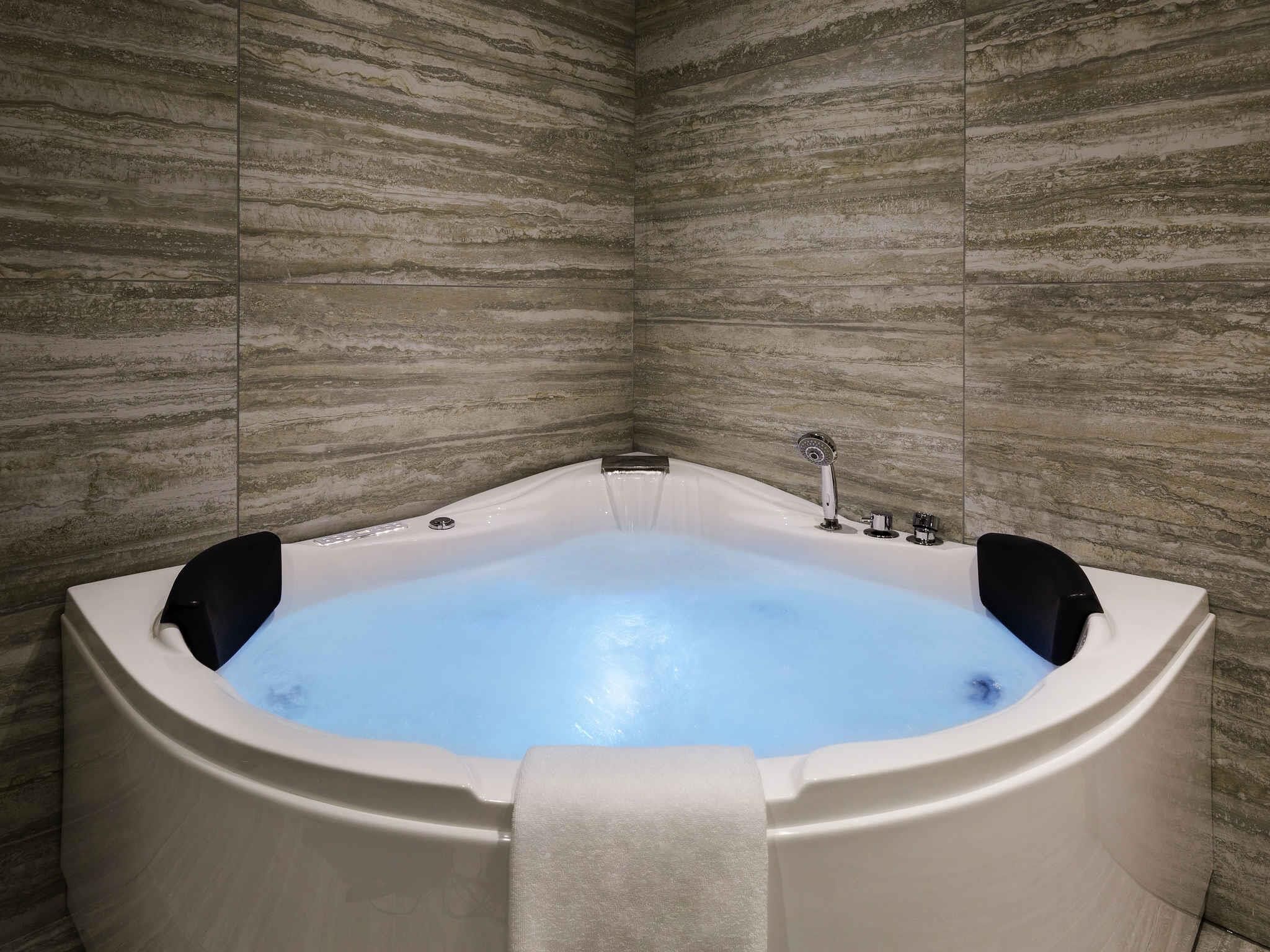A corner bathtub with a white interior, a black faucet, and a towel hanging on the side.