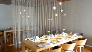 A dining area with a long table set for six, surrounded by chairs, and a curtain partially covering the window. - Novotel Jeddah Tahlia (Jeddah)