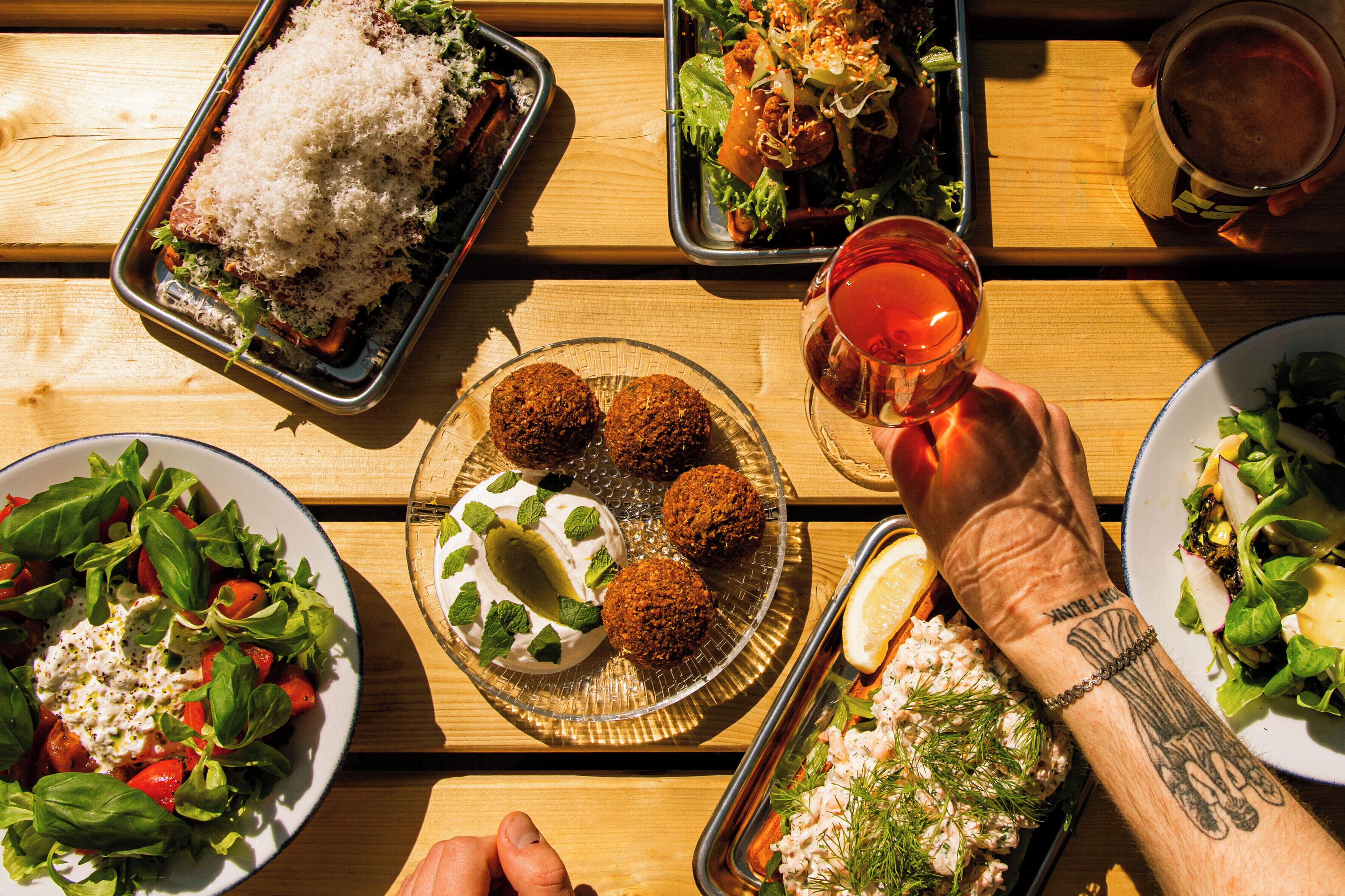 Una mesa de madera con varios platos, incluyendo una ensalada, una porción de falafel y una bandeja de comida.