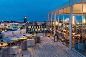A rooftop terrace with a sofa, round tables, and potted plants.
