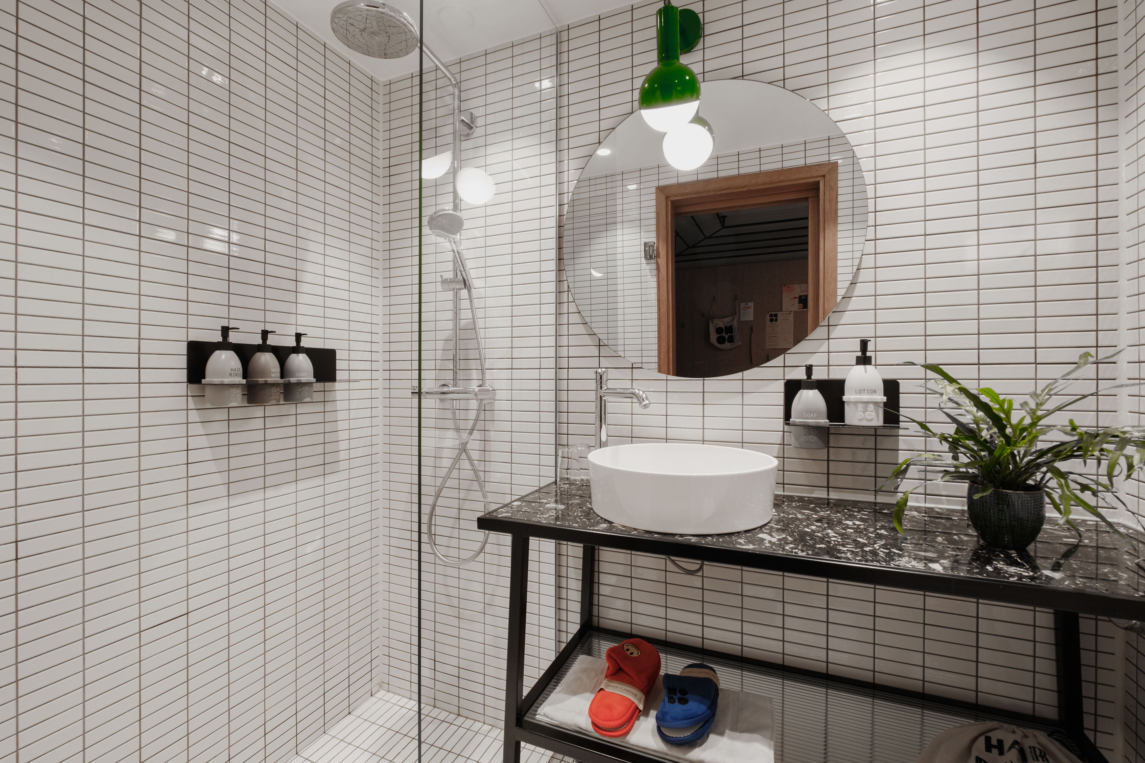 Un baño moderno con pared de azulejos blancos, encimera negra, lavabo redondo y espejo con marco de madera.