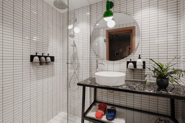 A modern bathroom with a white tiled wall, a black countertop, a round sink, and a mirror with a wooden frame.