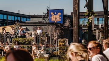An outdoor seating area with tables and chairs, a blue sign with yellow text, and a building in the background.