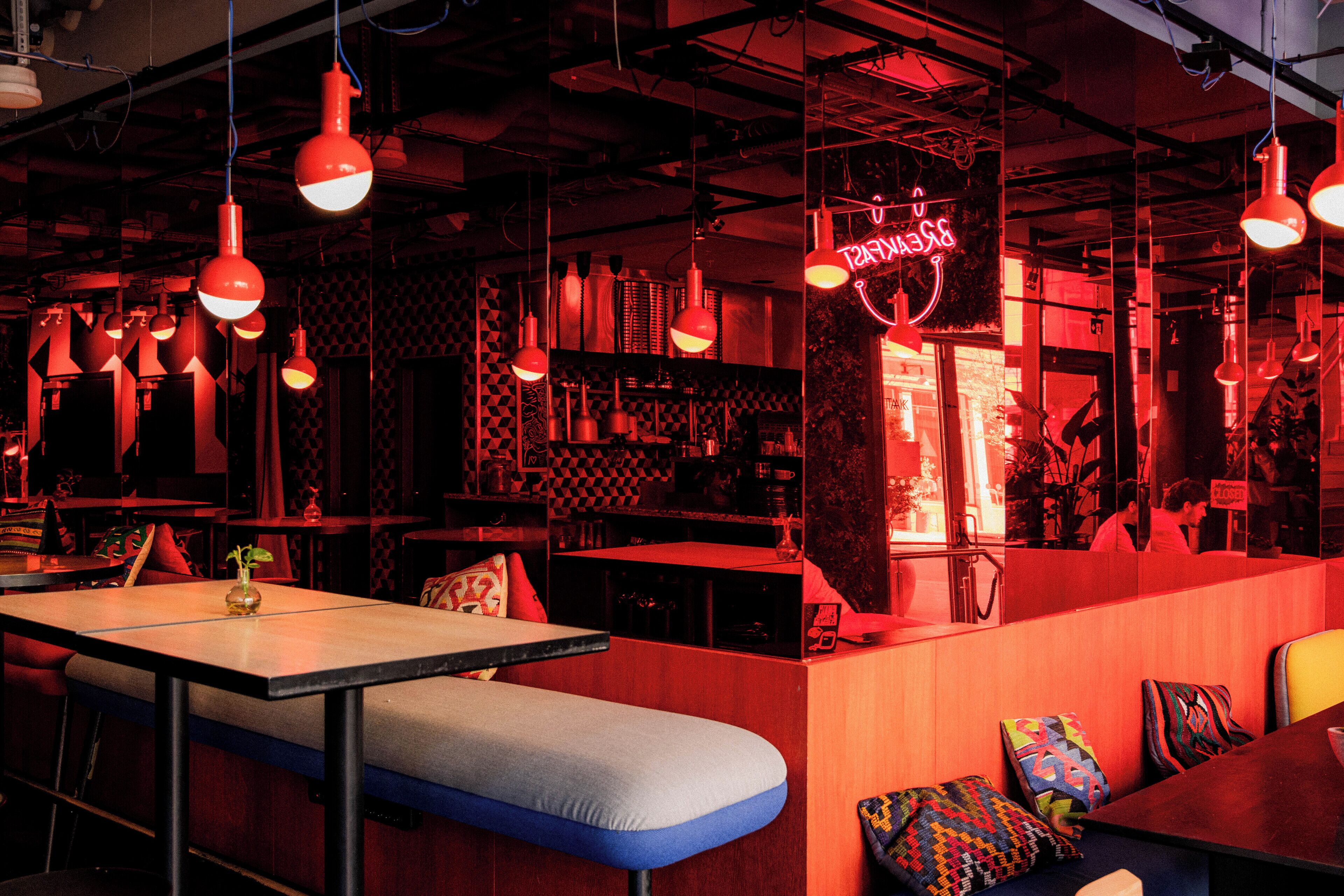 Un bar moderno con iluminación roja, cabinas y un letrero de neón.