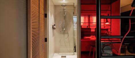 Un baño moderno con ducha de vidrio, zona de tocador con iluminación roja y una cocina visible al fondo.