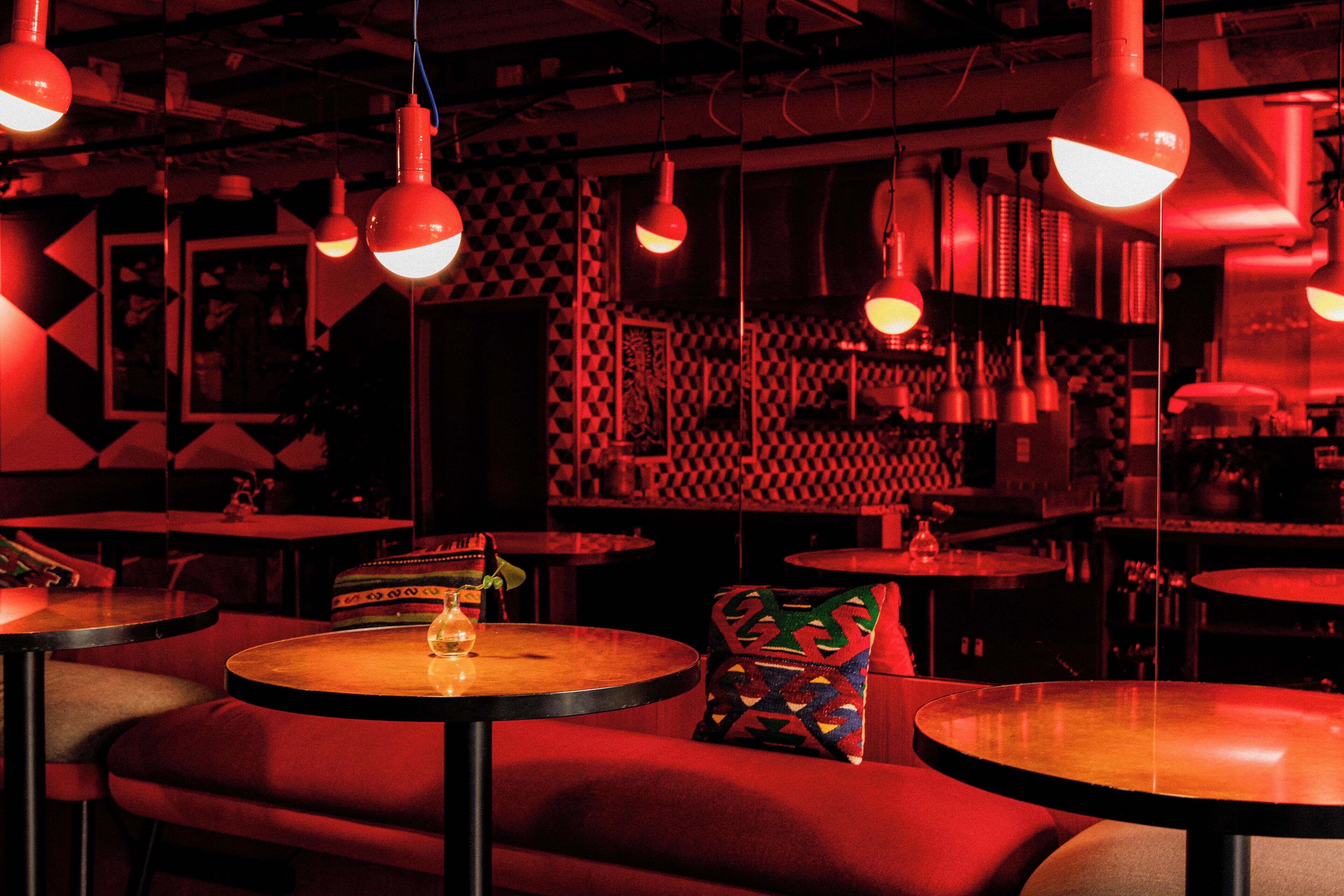 Un bar tenuemente iluminado con mesas redondas y asientos rojos.
