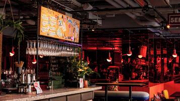 Una zona de bar con mostrador, taburetes y luces colgantes.