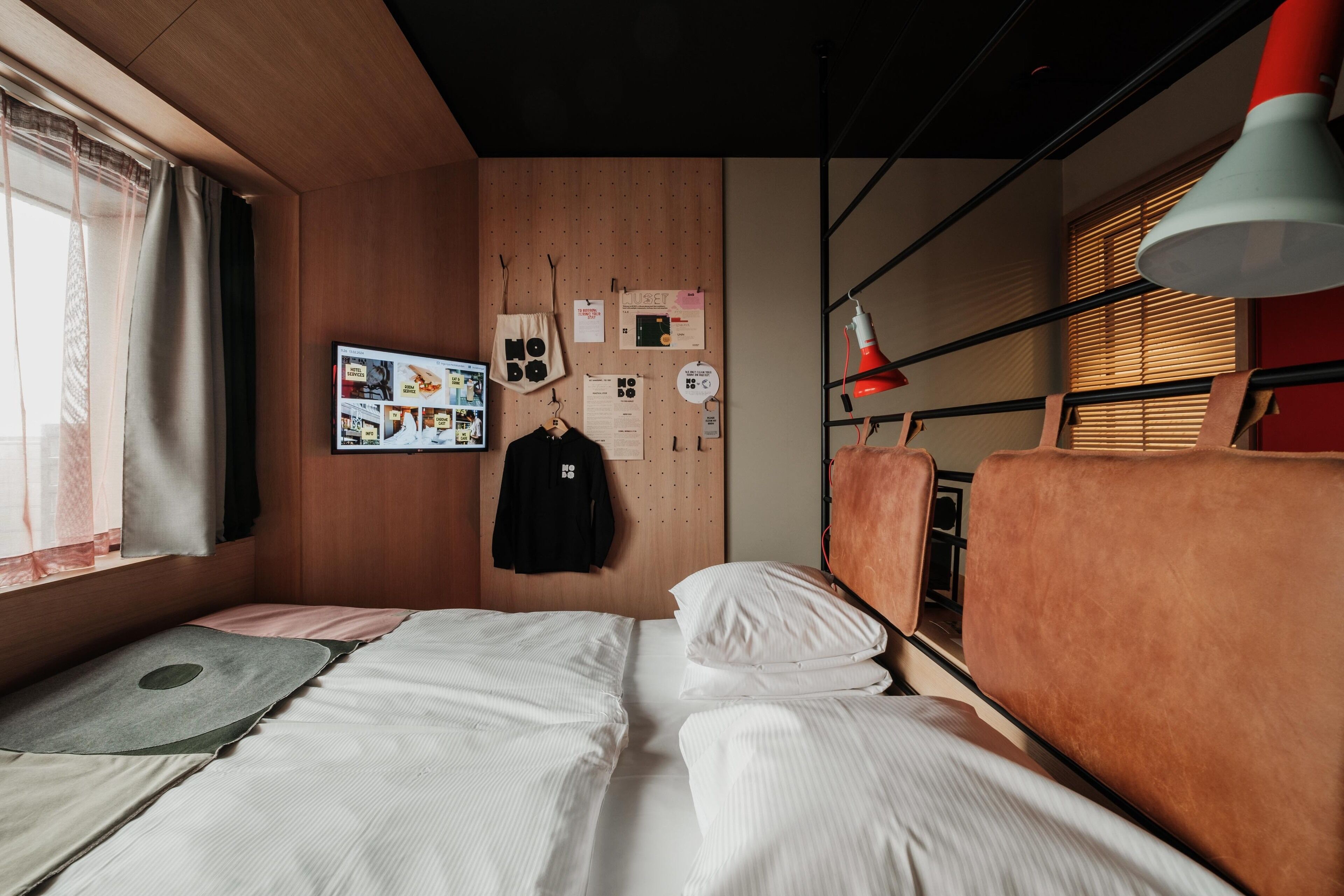 A room with two beds, a wooden wall with various items, a red lamp, and a window with curtains.