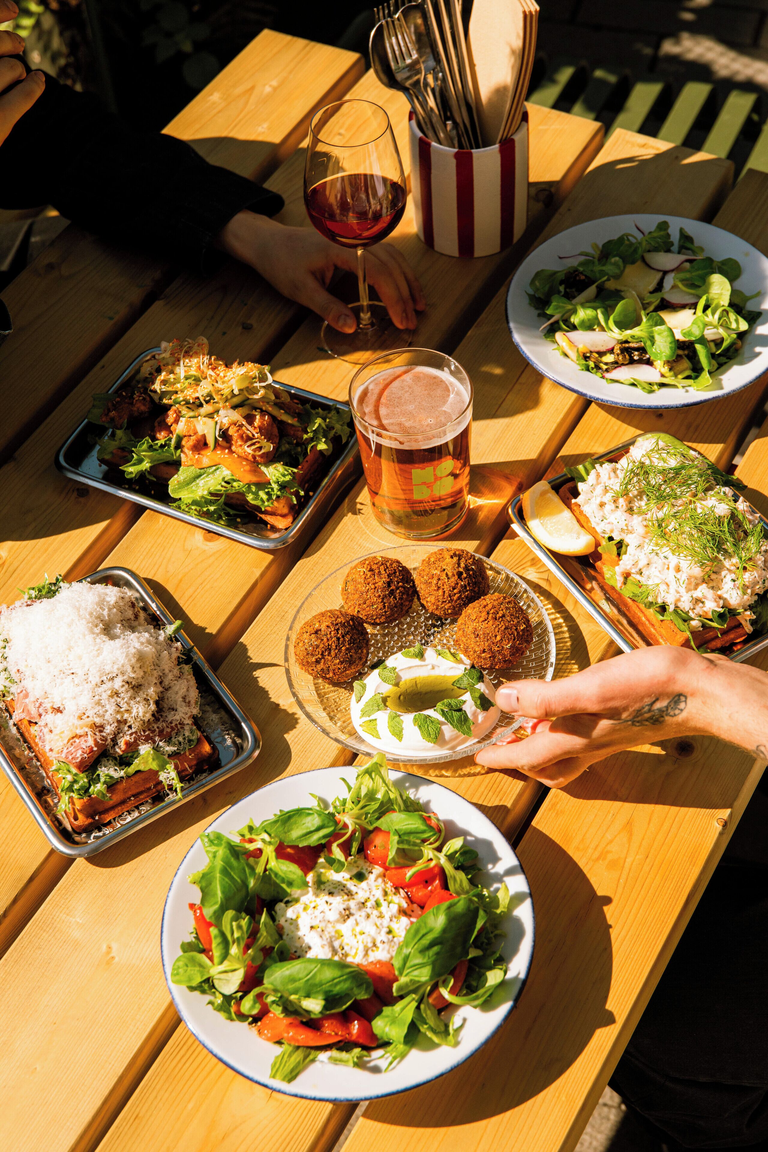 Une table en bois sur laquelle on trouve différents plats, notamment des salades, une boisson et une assiette de falafels.
