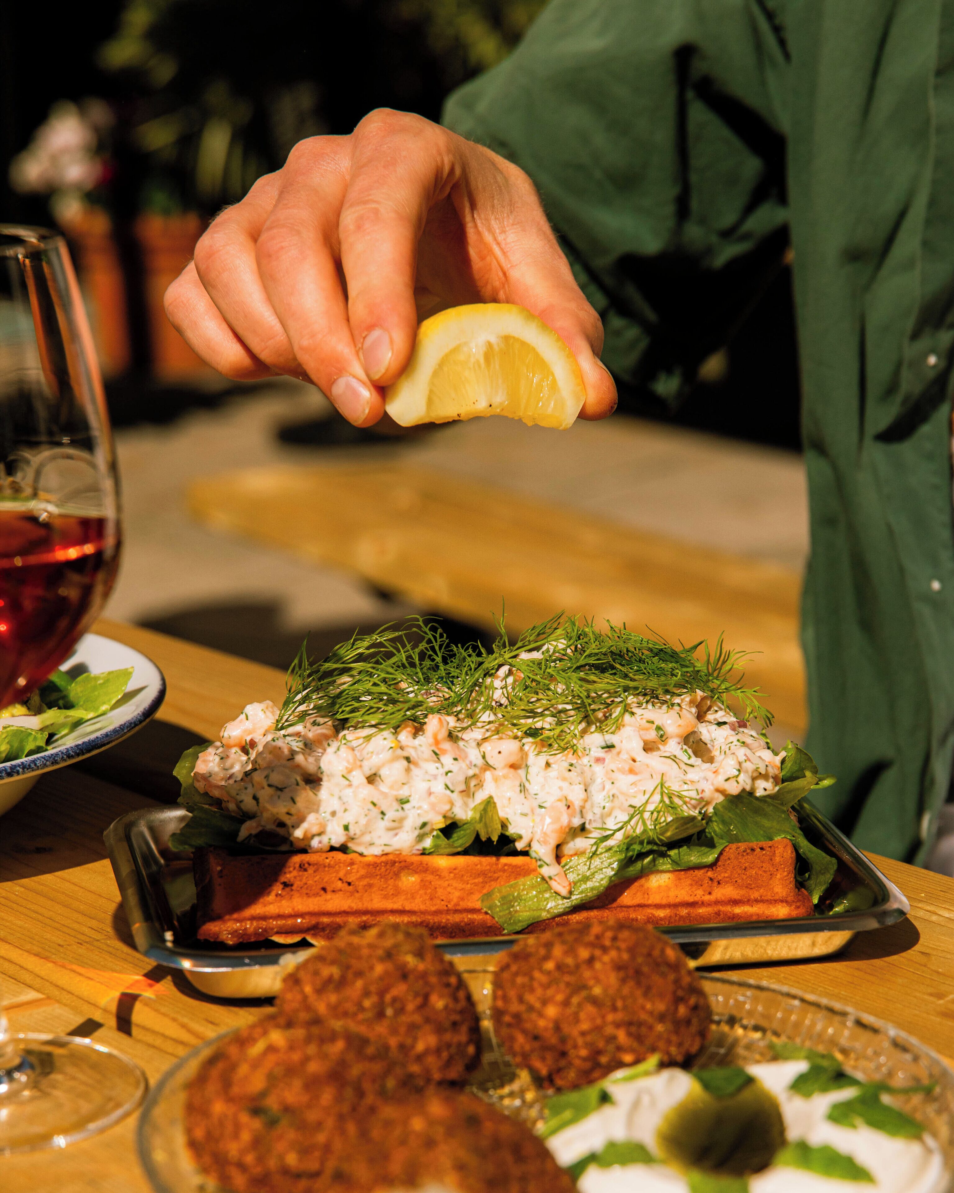 A person holding a lemon over a dish of food, possibly at a restaurant.
