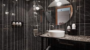 Un baño moderno con paredes de azulejos negros, un lavamanos redondo blanco y un espejo grande.