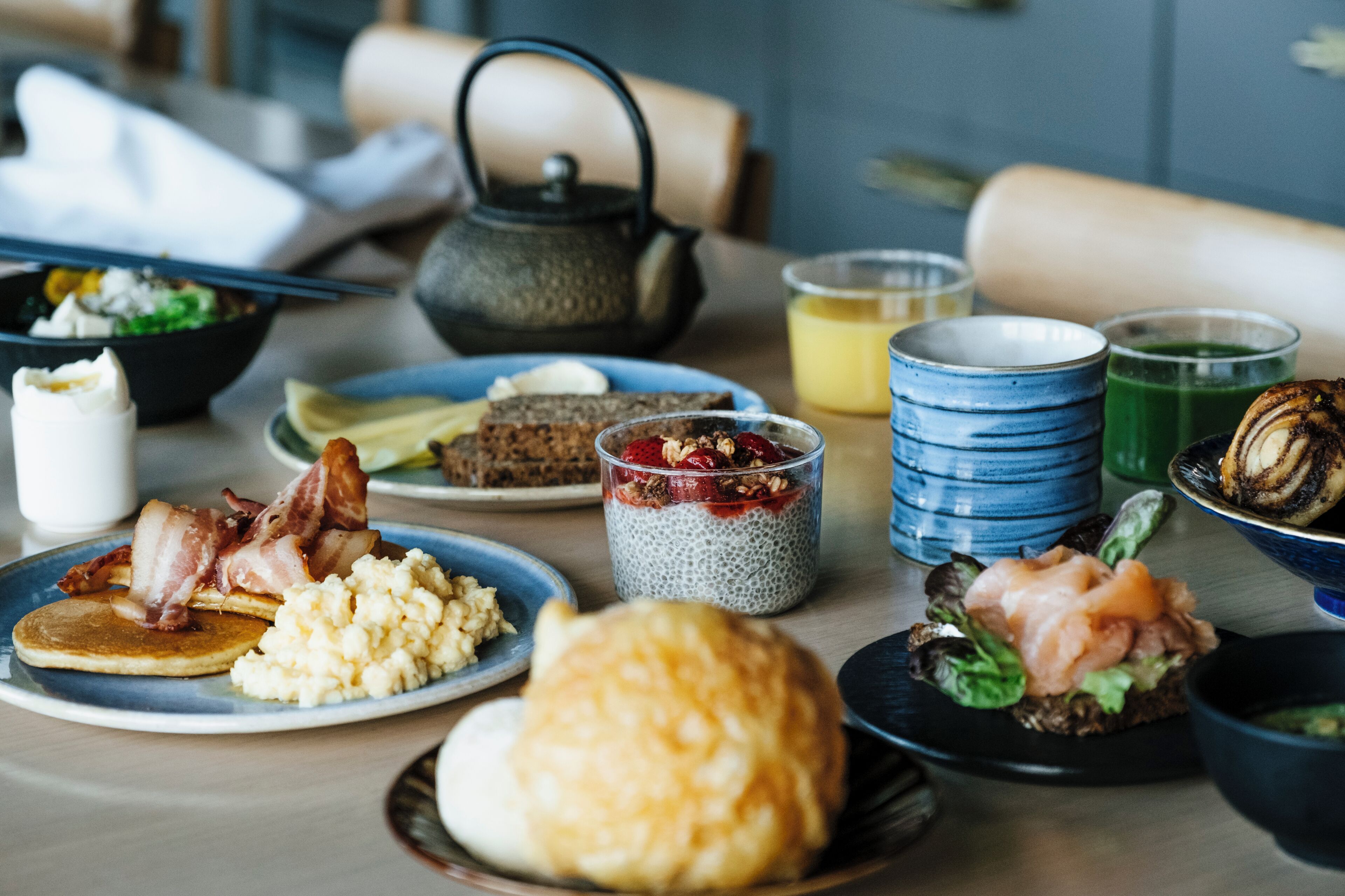 A breakfast table with various dishes including pancakes, bacon, and a green smoothie.
