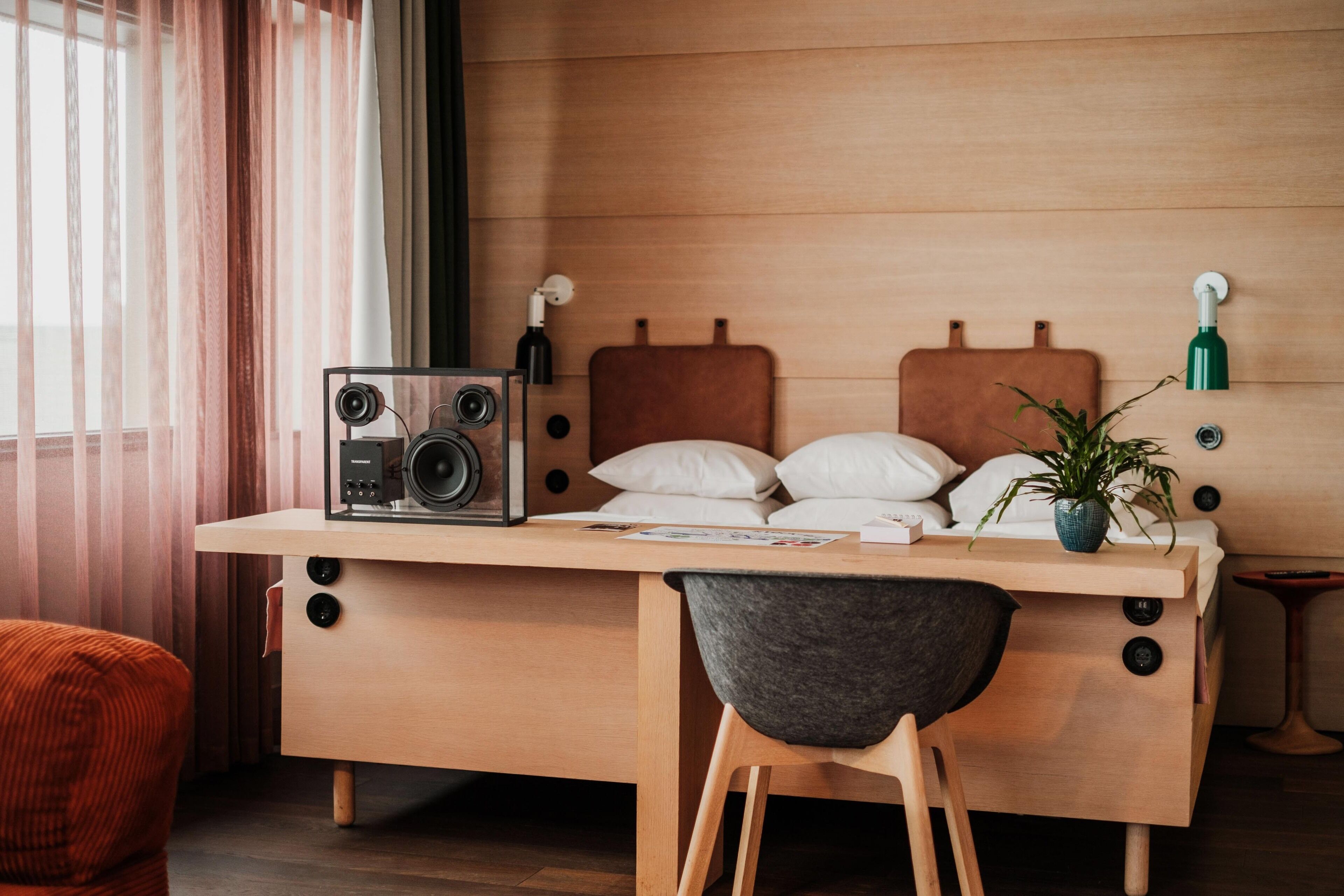 A modern bedroom with a wooden bed, a desk with a radio, a chair, and a potted plant.