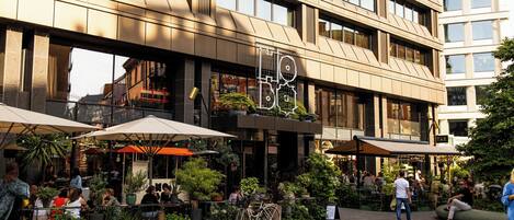 Un edificio moderno con un área de café que ofrece mesas al aire libre y plantas en macetas.