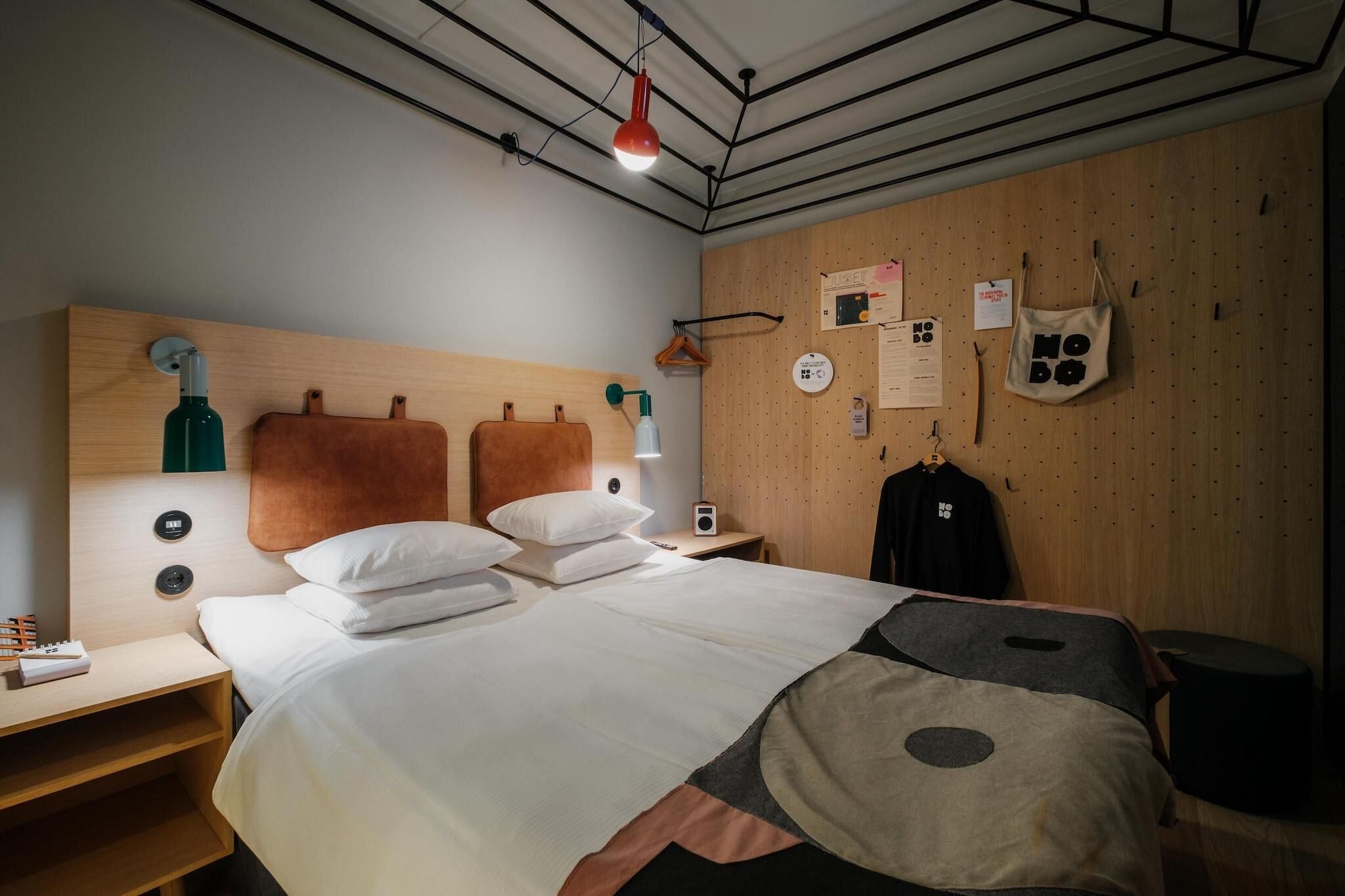 Une chambre d’hôtel avec une tête de lit en bois, un lit avec une literie blanche, une table de chevet avec une lampe, une radio et un porte-bagages fixé au mur.