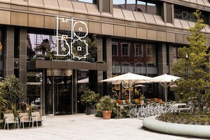 A modern building with a large entrance, outdoor seating area with umbrellas, and bicycles parked outside.