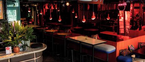 Interior de restaurante con cabinas, mesas y lámparas colgantes rojas.