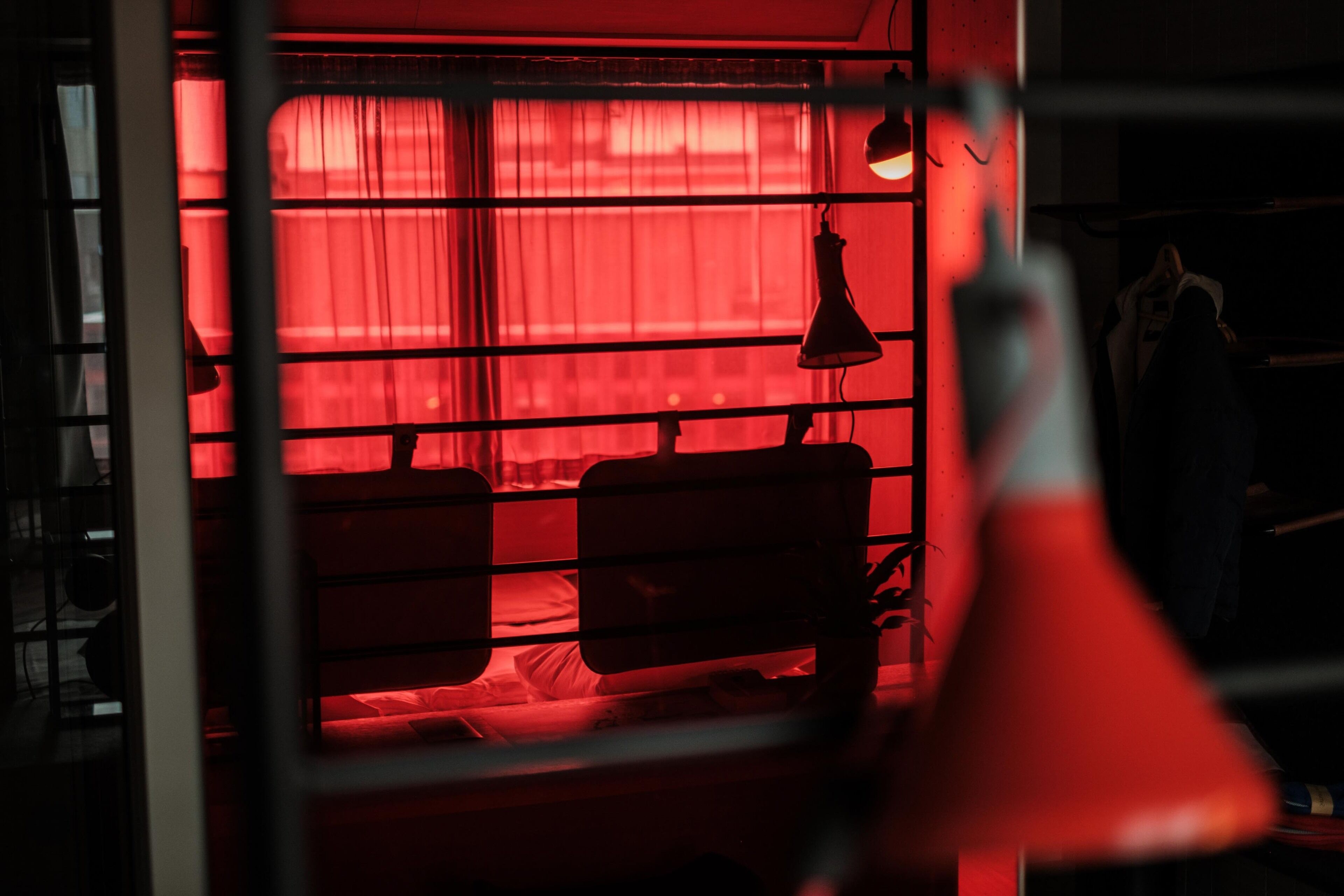 A room with a red-lit window, a hanging lamp, and a bed.