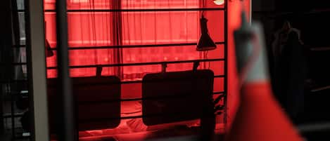 A room with a red-lit window, a hanging lamp, and a bed.