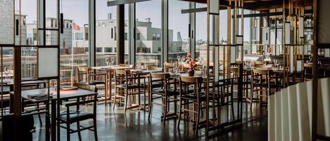 Un restaurante moderno con techos altos, ventanas amplias y vistas a la ciudad.
