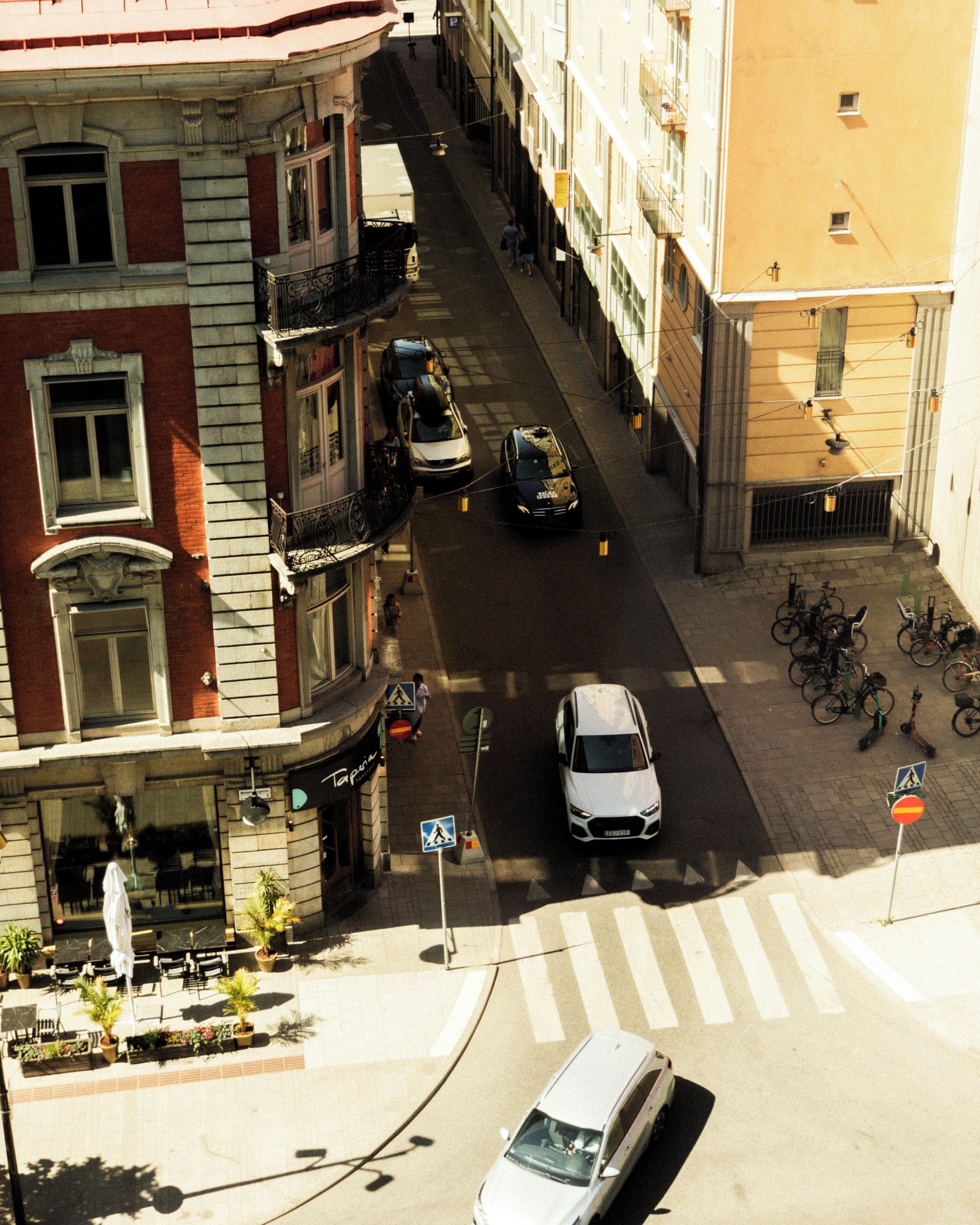 Vista de la calle con un coche blanco estacionado en un paso de peatones, edificios con balcones y bicicletas aparcadas en la acera.