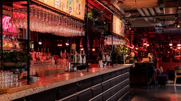 Un bar con una barra larga, estantes con vasos y un letrero de neón.