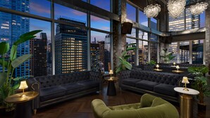 Um lounge moderno com sofás escuros, mesas redondas e amplas janelas com vista para a cidade.