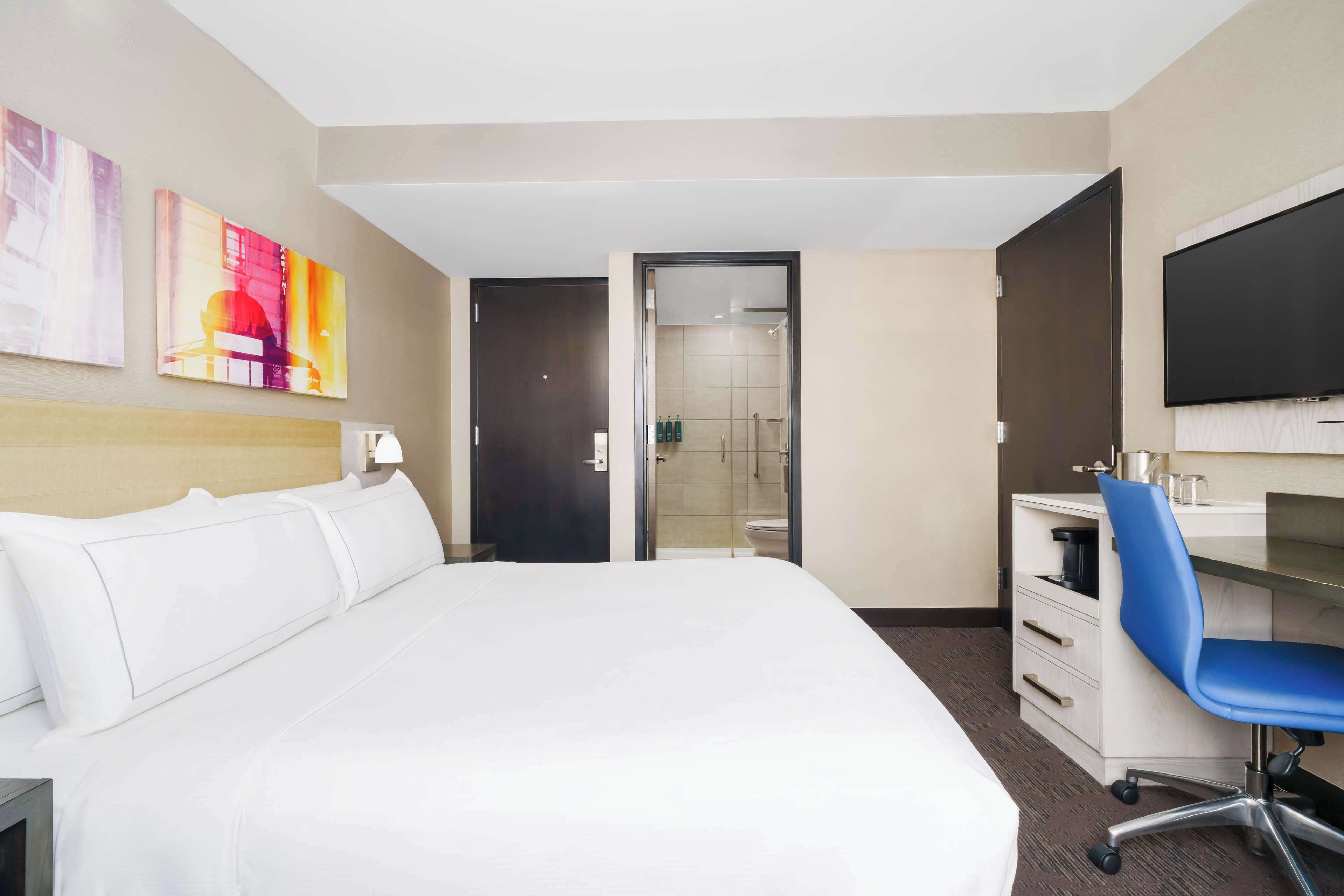 Habitación de hotel con una cama grande, un escritorio con una silla, un televisor y obras de arte en la pared.