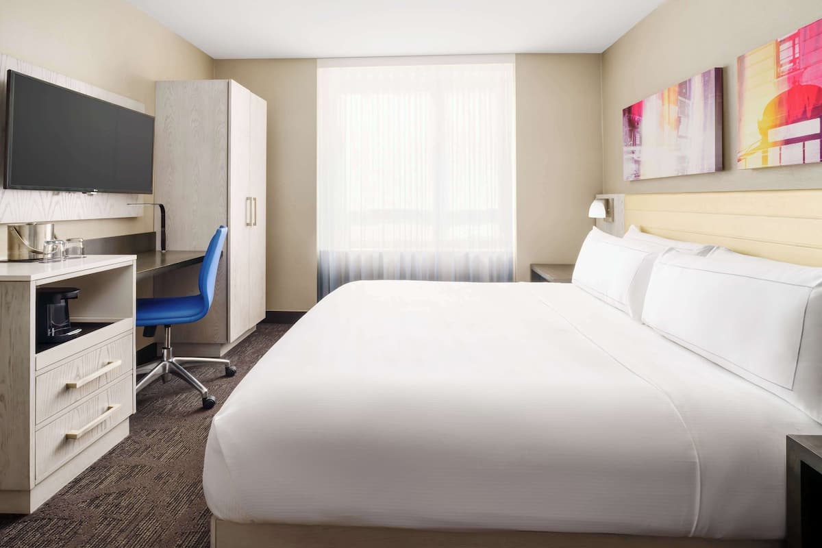 Quarto de hotel com uma cama grande, uma mesa com cadeira, televisão e obras de arte na parede.
