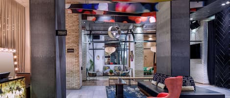 A modern hotel lobby with a reception desk, seating area, and a view of the kitchen in the background.