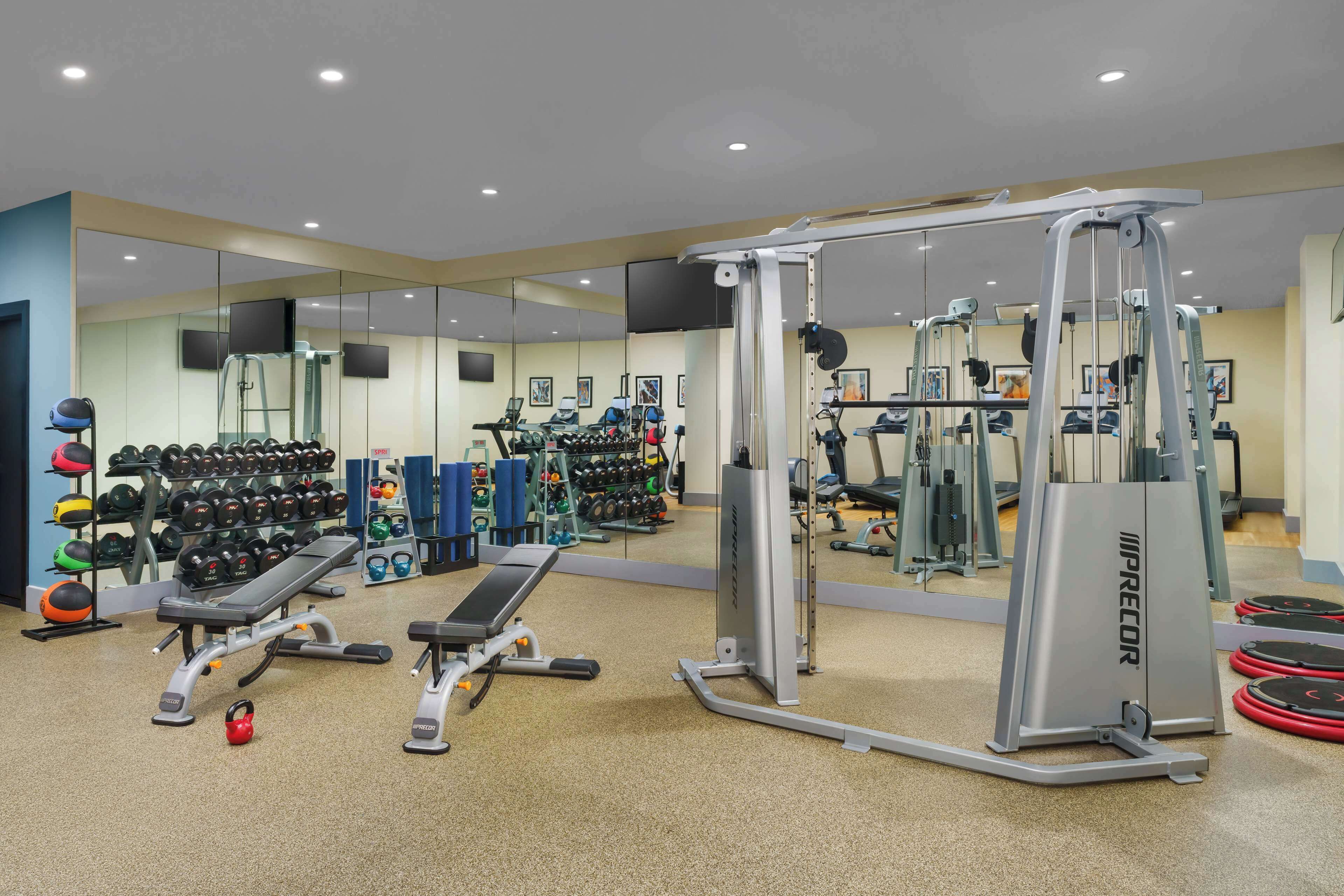 Een fitnessruimte met diverse trainingsapparaten, waaronder een bankje, kettlebells, dumbbells en een kabelmachine.
