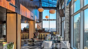 Uma área de estar moderna com assentos, bar e grandes janelas com vista para a cidade.