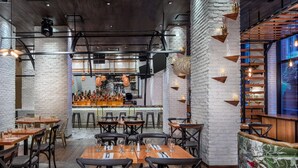 Interior de restaurante com paredes de tijolo, mesas de madeira e luminárias pendentes.