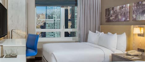 A hotel room with two beds, a desk, a chair, a TV, a window with a city view, and artwork on the wall.