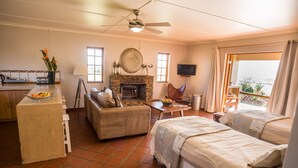 A cozy room with a fireplace, a TV, a dining area, and a balcony with a view. - Kwetu Guest Farm (Swellendam)