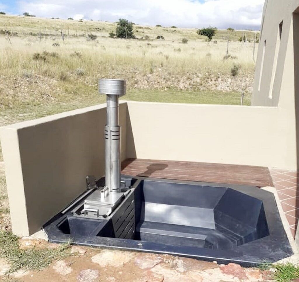 Ein modernes Outdoor-Whirlpool mit einem Metallschornstein, vor einer grünen Wiese und einem Gebäude.