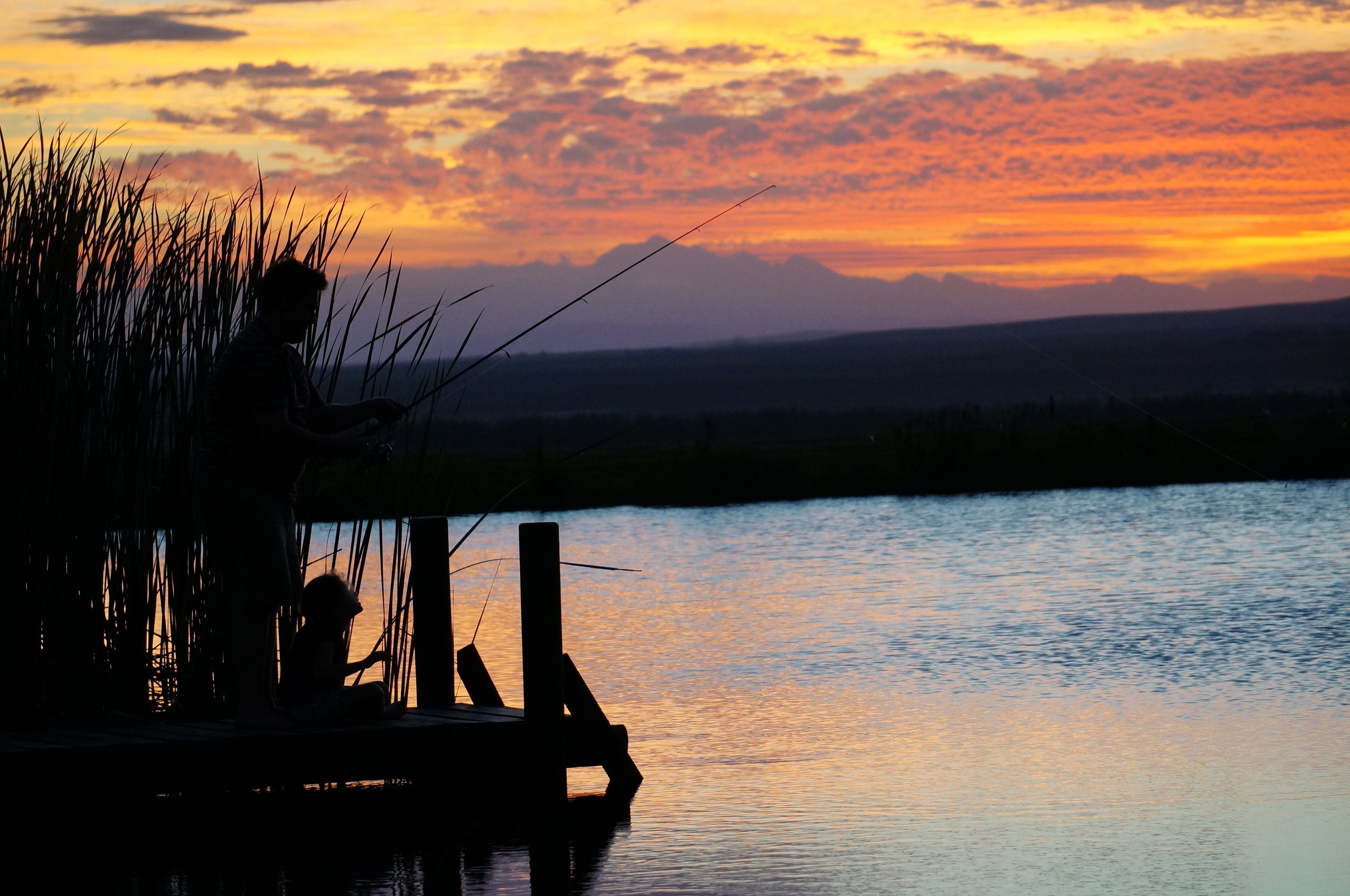 A silhouette of a person fishing at dusk with a sunset in the background.