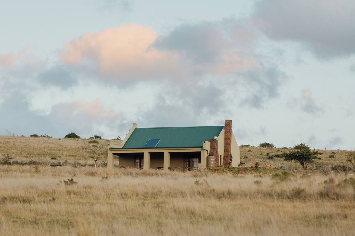 A house with a green roof, solar panels, and a brick chimney, surrounded by a grassy landscape.