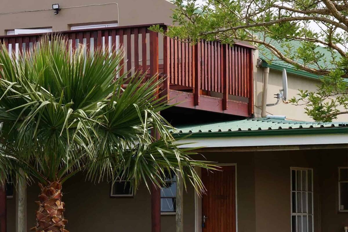 A residential building with a balcony, a palm tree, and a green roof.