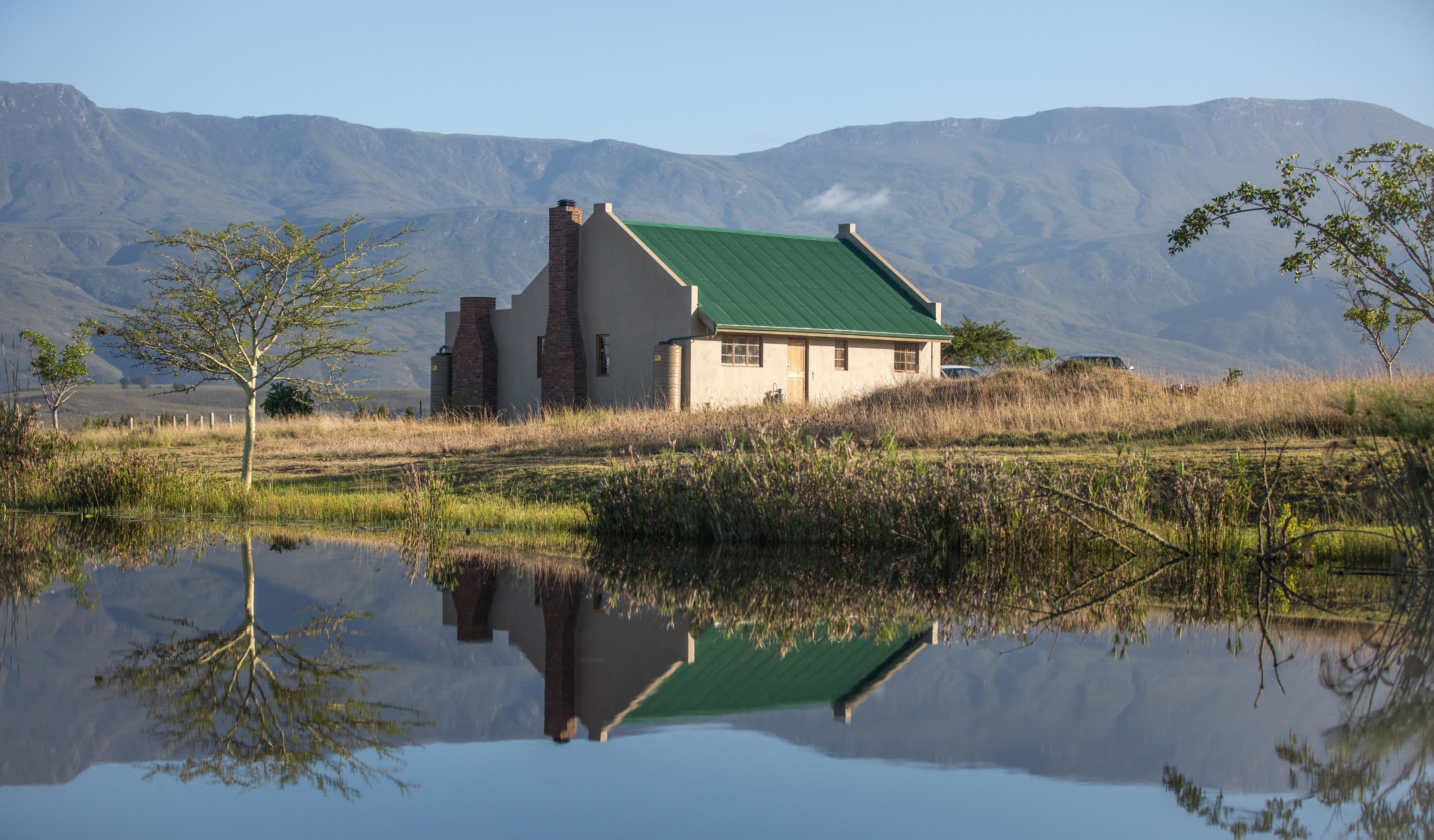 Une maison avec un toit végétalisé, une cheminée en briques et son reflet dans une étendue d’eau.