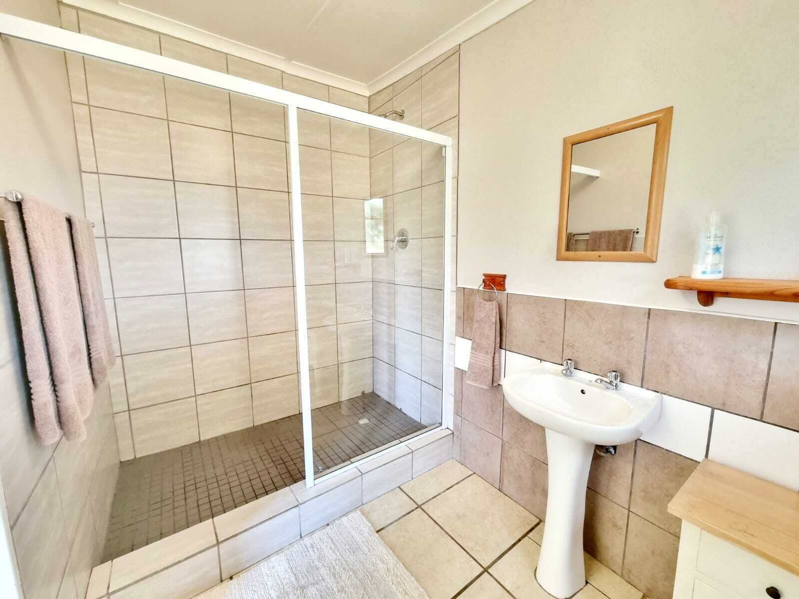 Een moderne badkamer met een douchecabine van glas, een wit wastafeltje op voet en een houten opbergmeubel.