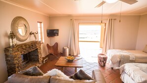 A cozy room with a stone fireplace, leather sofa, a dining table with fruit, and a bed. - Kwetu Guest Farm (Swellendam)