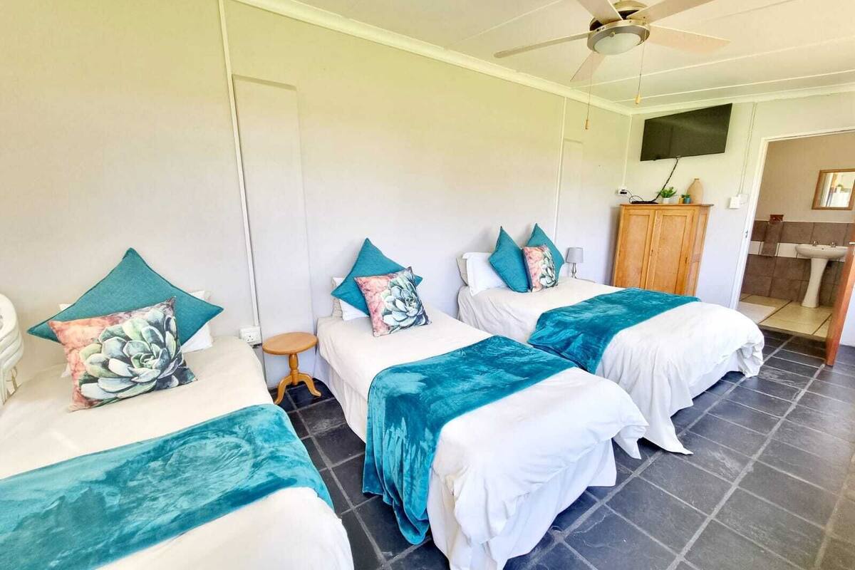 A hotel room with two beds, a ceiling fan, a TV, a wooden cabinet, and a bathroom visible through an open door.