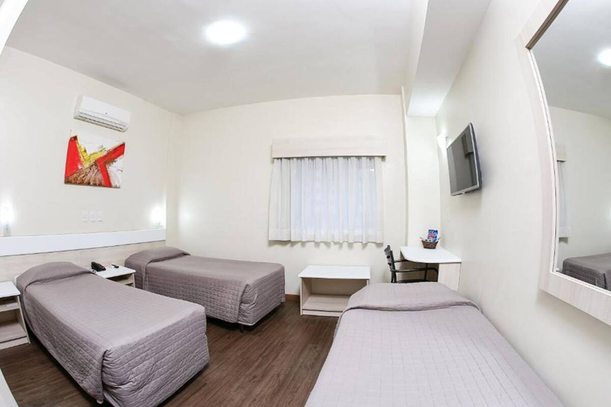 A hotel room with two single beds, a small desk, a chair, a TV, and a window with curtains.