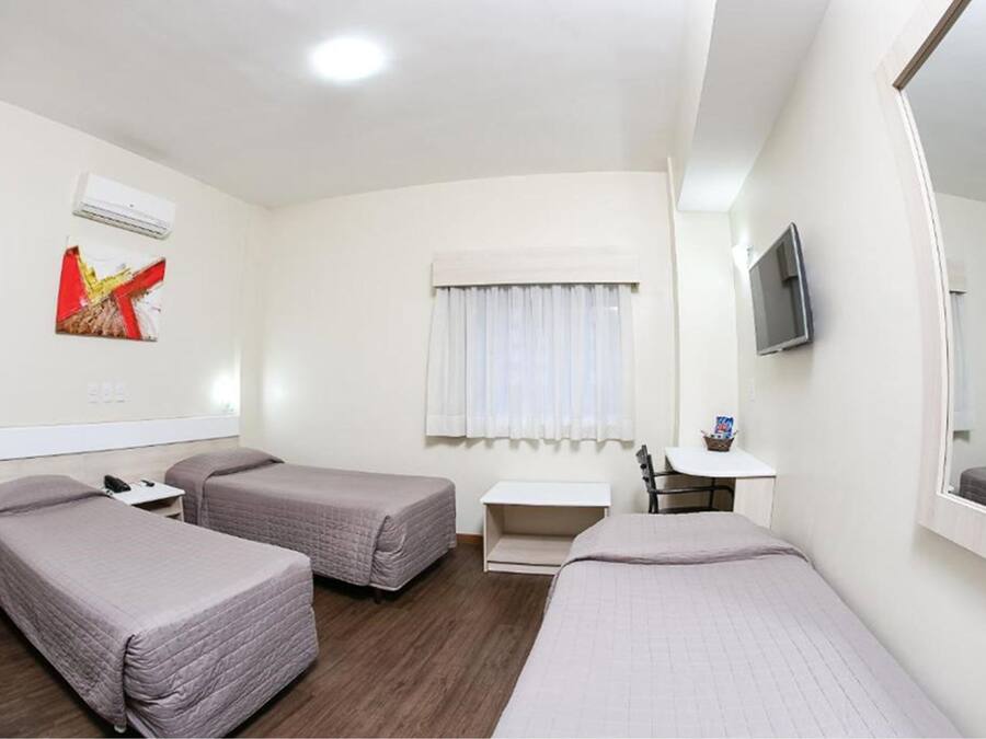 A hotel room with two single beds, a small desk, a chair, a TV, and a window with curtains.